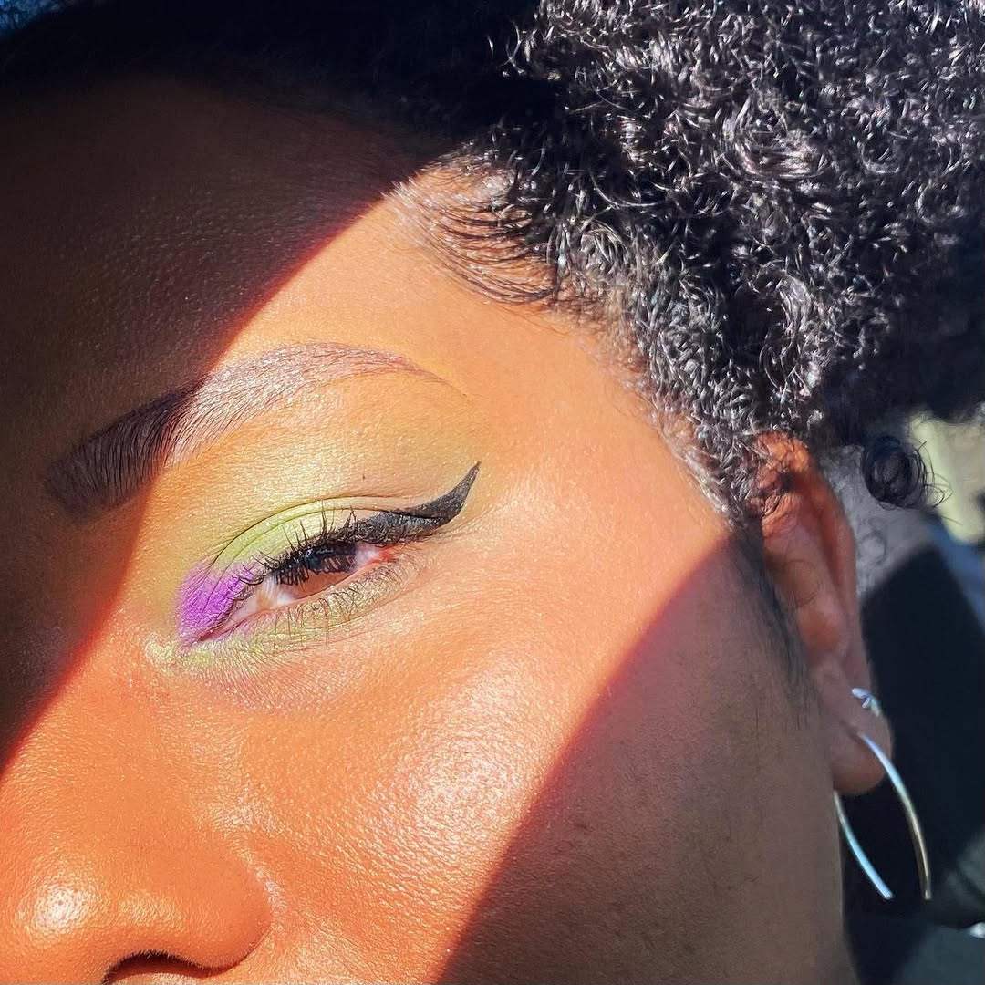 Close-up of a person with colorful eye makeup and a black hat.