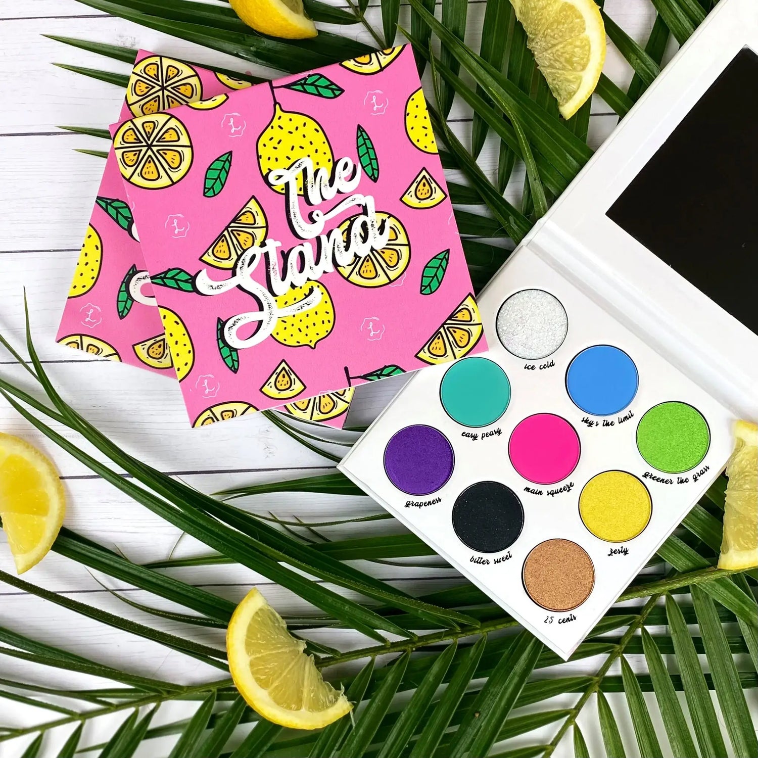 Makeup palette with colorful shades and a pink pouch with fruit pattern on a leafy background