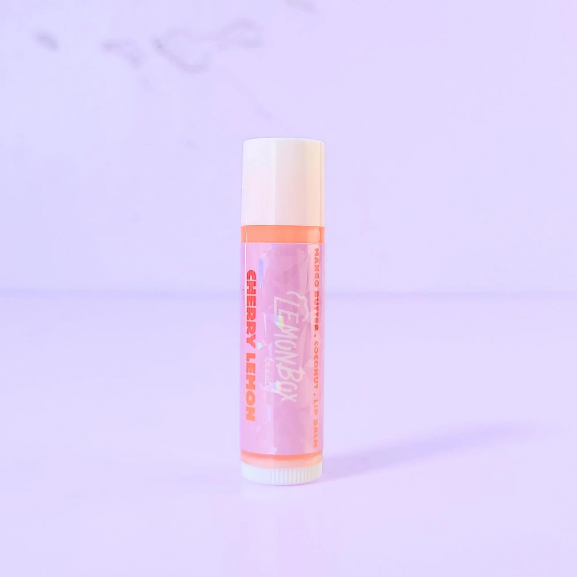 Lemon Box Beauty Cherry Lemon Lip Balm - Mango Butter and Vitamin E infused hydrating balm tube on a lavender background.