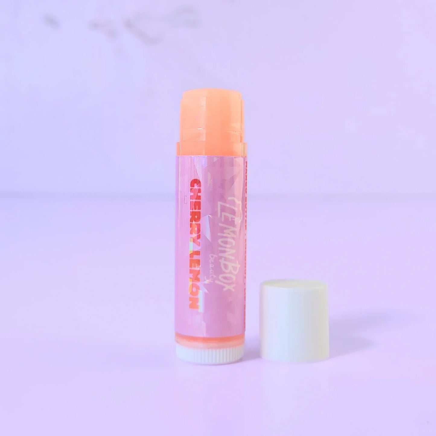 Lemon Box Beauty Cherry Lemon Lip Balm - Mango Butter and Vitamin E infused hydrating balm tube on a lavender background.