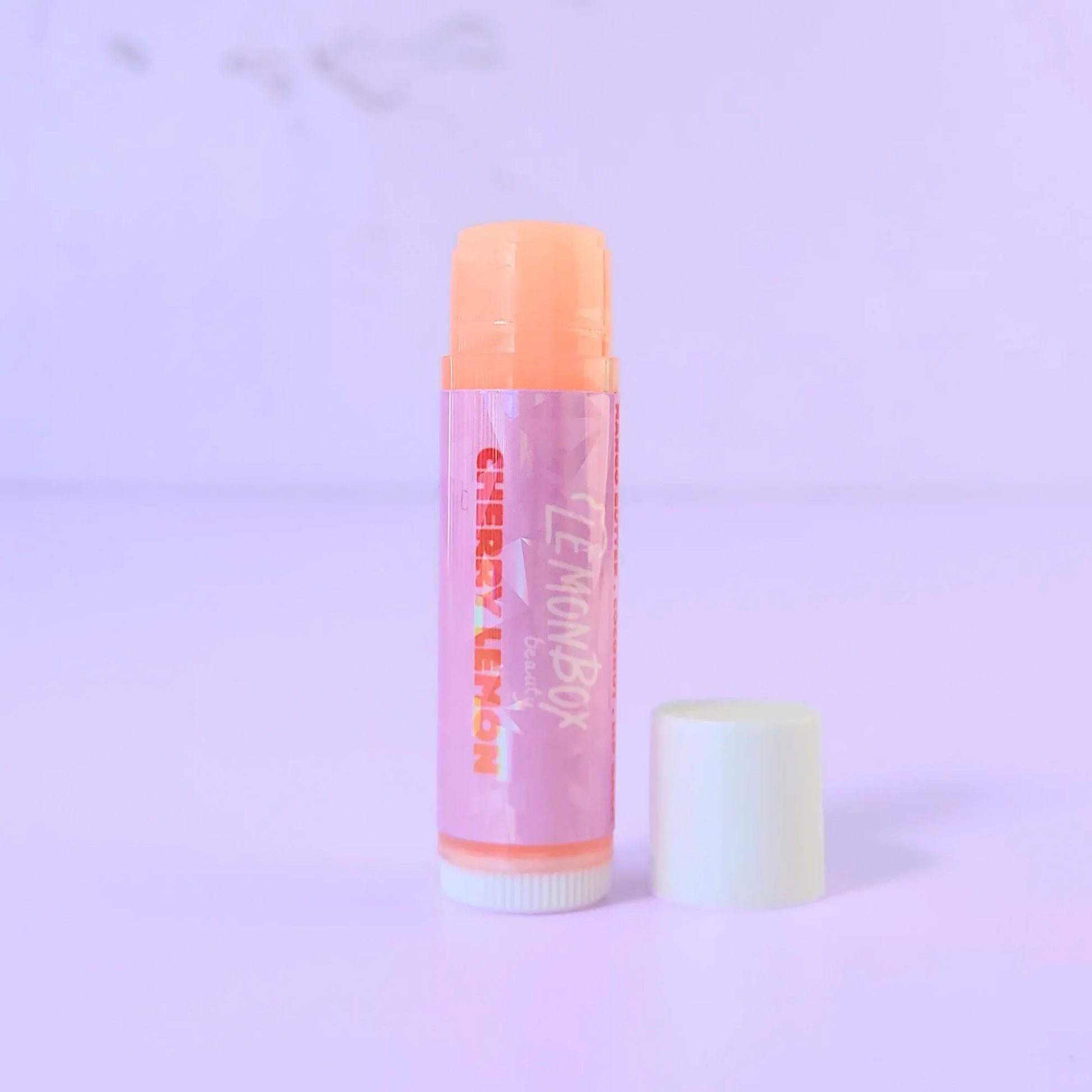 Lemon Box Beauty Cherry Lemon Lip Balm - Mango Butter and Vitamin E infused hydrating balm tube on a lavender background.