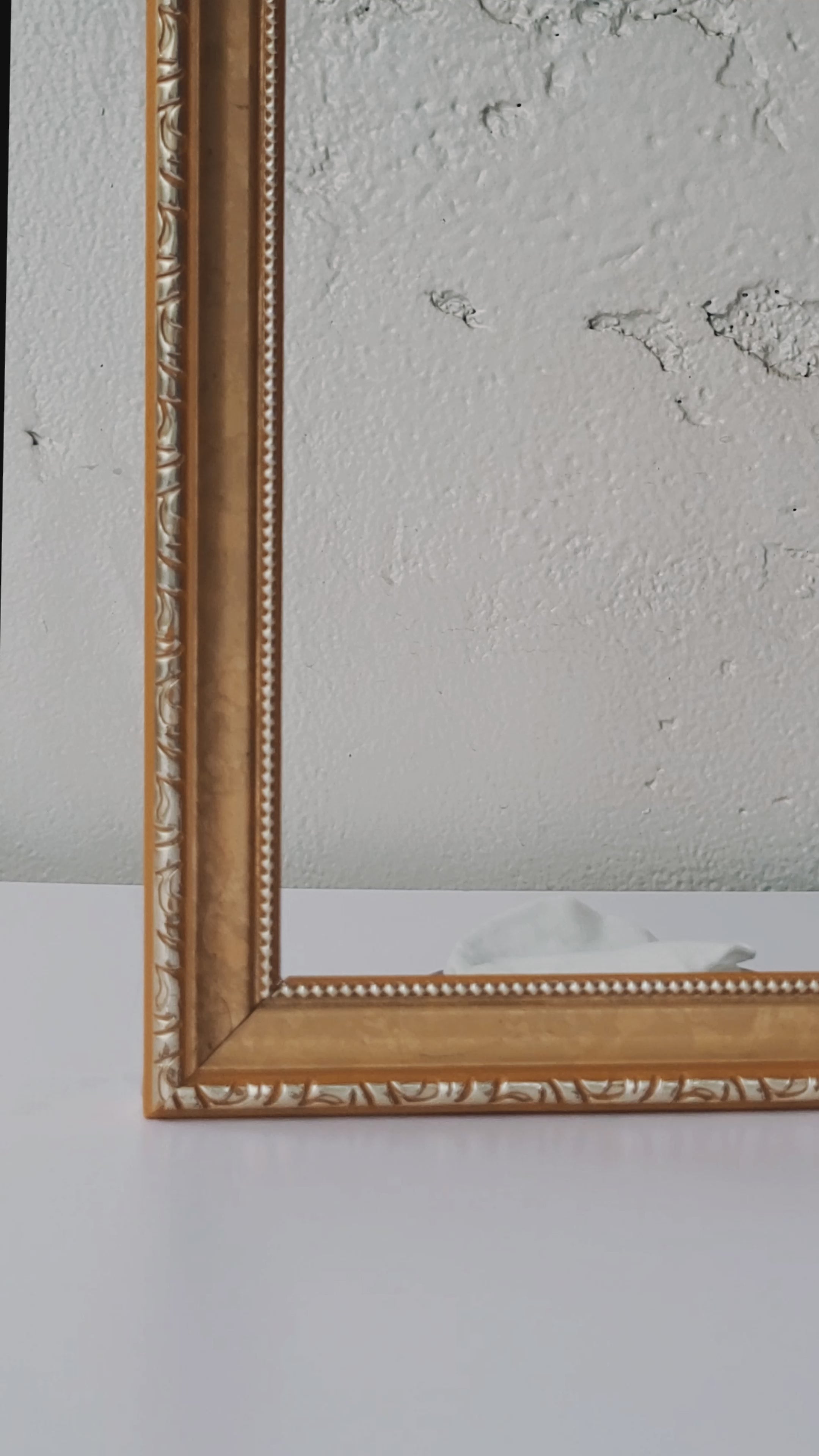 Decorative gold-framed mirror reflecting a stack of white exfoliating toner pads