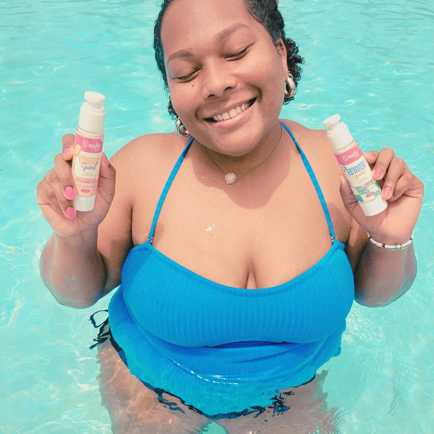 Woman in a blue swimsuit holding two bottles of sunscreen in a pool.