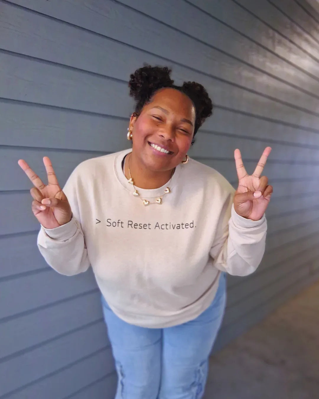 Person wearing a sweatshirt with 'Soft Reset Activated' text, making peace signs.