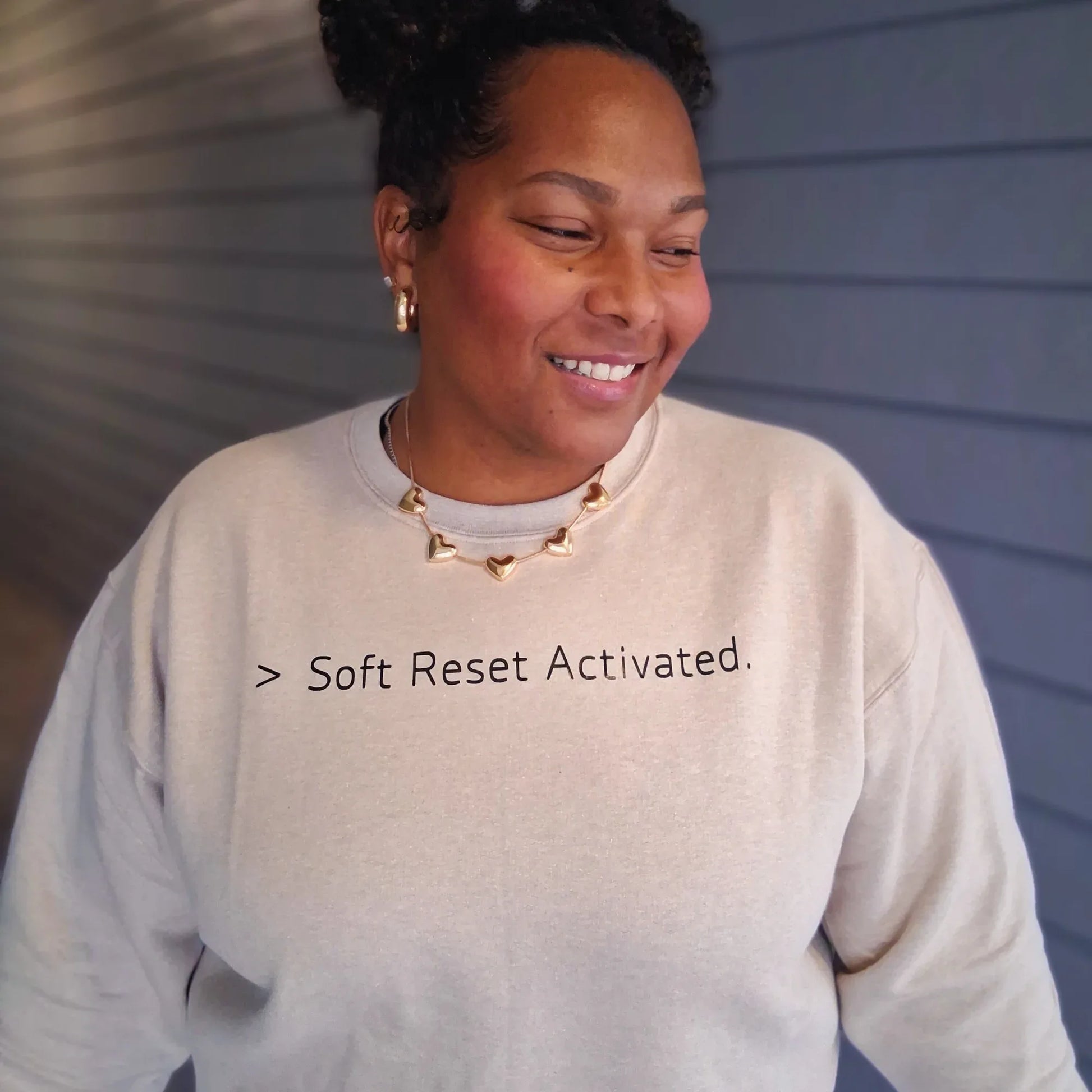 Person wearing a light-colored sweatshirt with text '> Soft Reset Activated.' against a neutral background