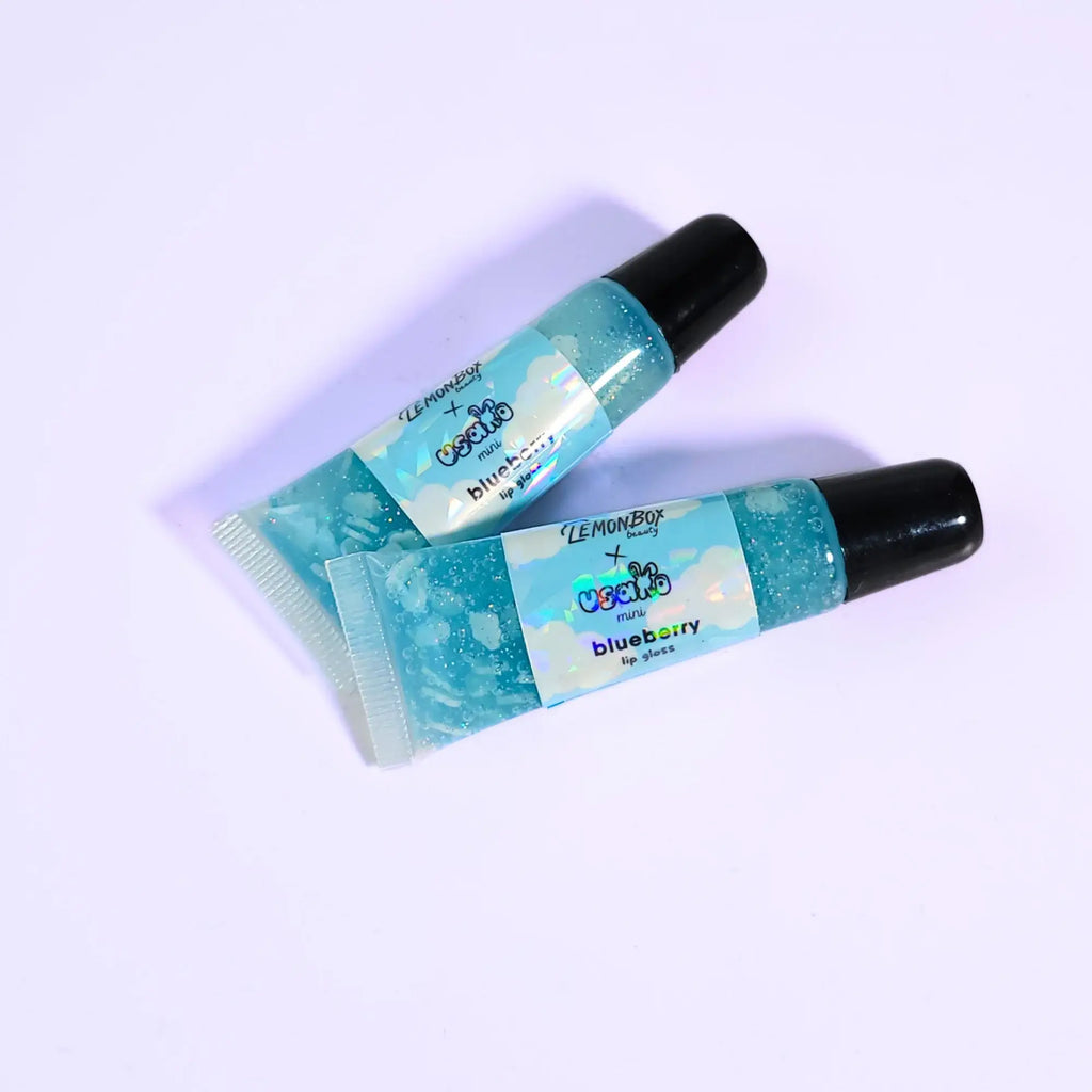 Two blueberry-flavored lip gloss on a light purple background