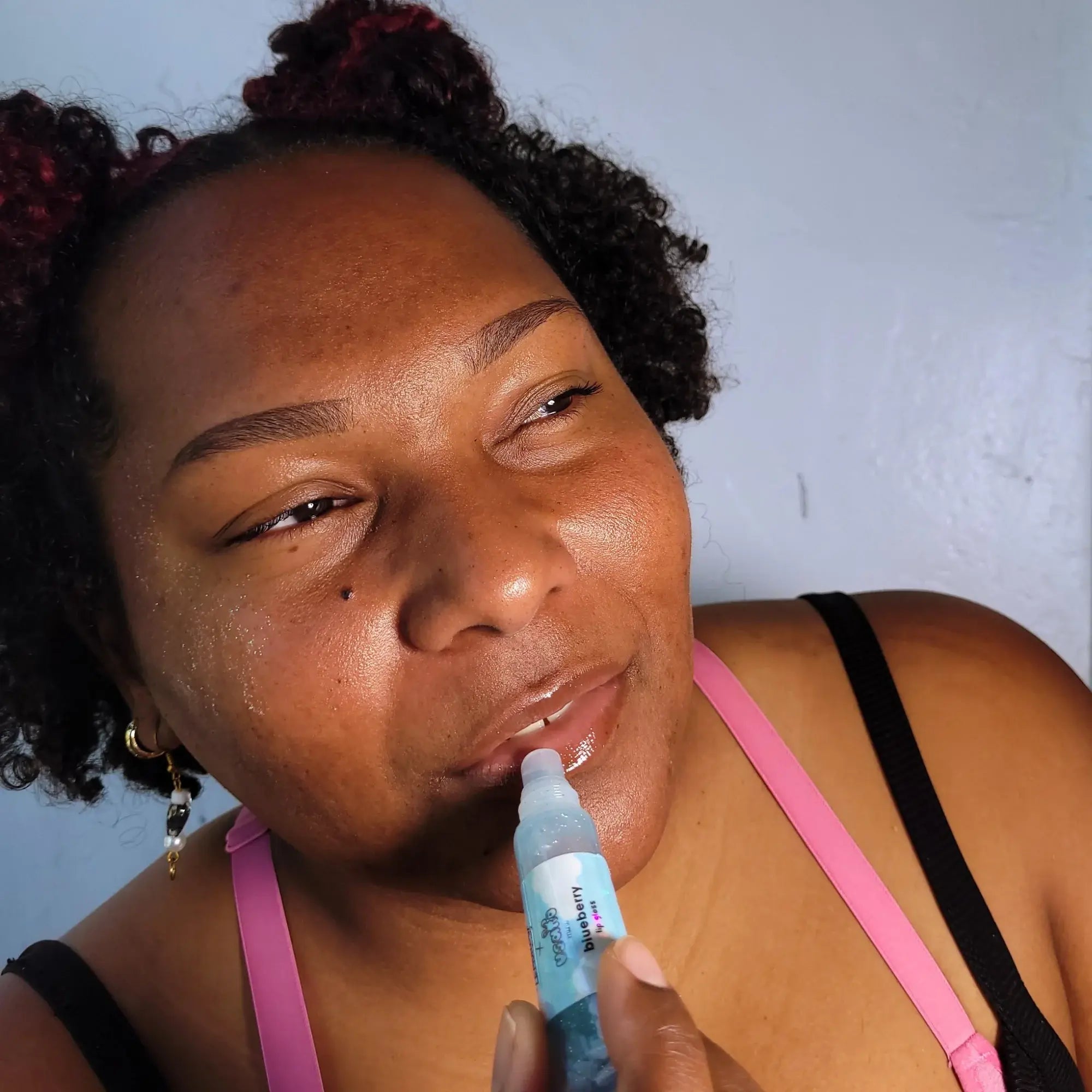 Woman applying lip balm with a blue tube against a light blue wall.